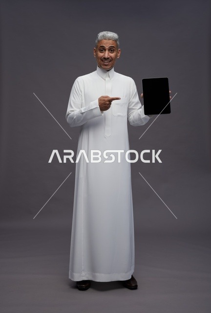 رجل سعودي يحمل جهاز لوحي أمام خلفية رمادية