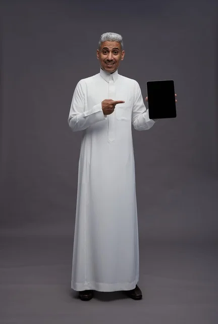 رجل سعودي يحمل جهاز لوحي أمام خلفية رمادية