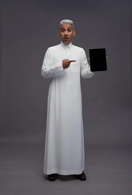 رجل سعودي يحمل جهاز لوحي أمام خلفية رمادية