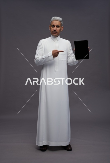 Saudi Man in Thobe Holding Tablet on Grey Background