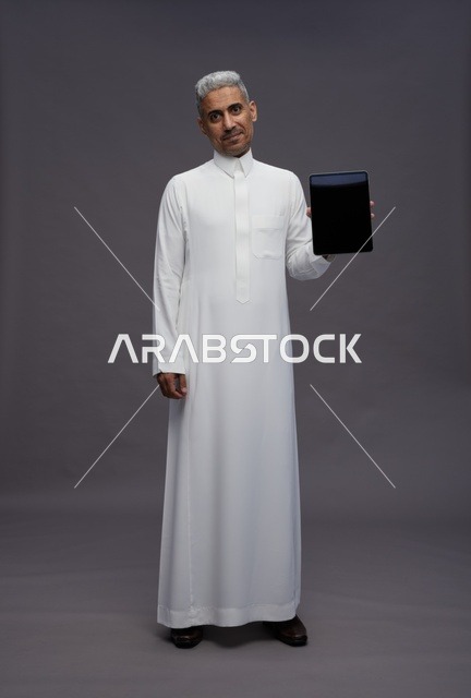رجل سعودي بالثوب يحمل جهاز لوحي شاشة سوداء