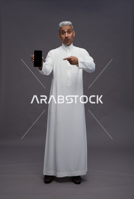 Saudi Man in White Thobe Holding Smartphone Surprised