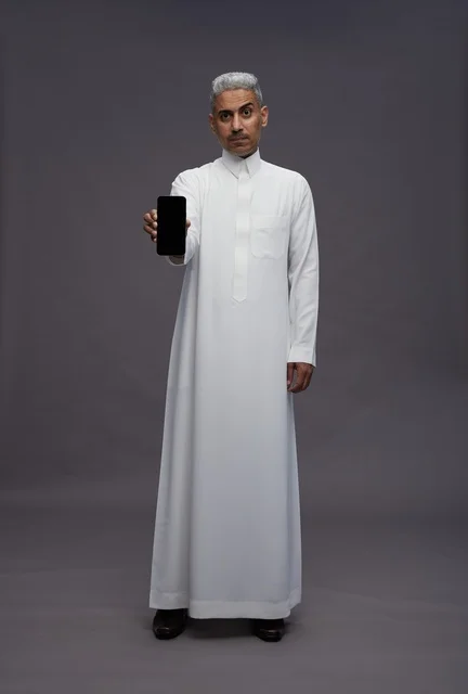 رجل سعودي بالثوب يعرض هاتفاً ذكياً شاشة فارغة