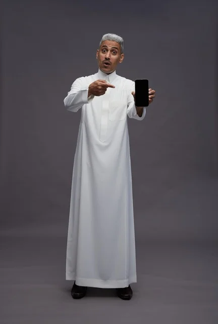 رجل سعودي يشير إلى هاتف ذكي في استوديو