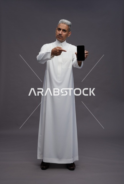 رجل سعودي بالثوب يشير إلى شاشة الهاتف الذكي