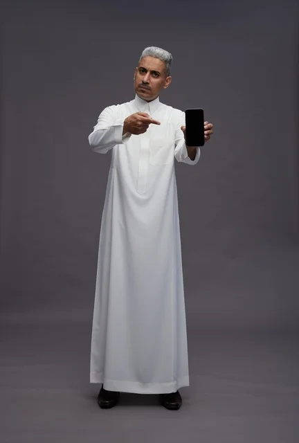 رجل سعودي بالثوب يشير إلى شاشة الهاتف الذكي