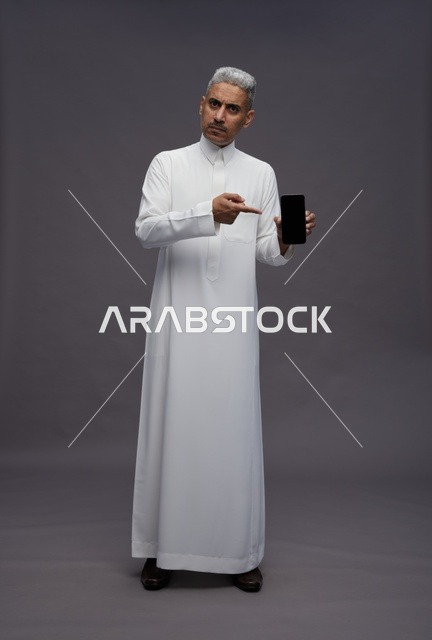 رجل سعودي يشير إلى شاشة هاتف ذكي في الاستوديو