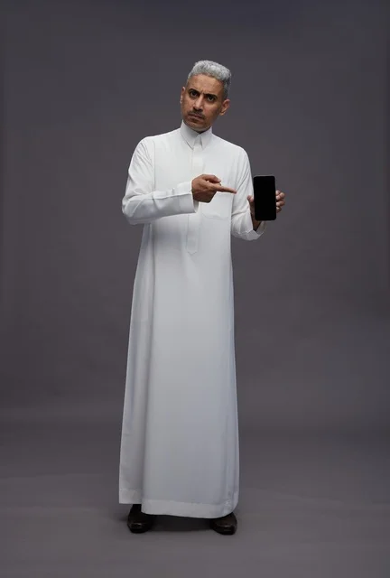 رجل سعودي يشير إلى شاشة هاتف ذكي في الاستوديو