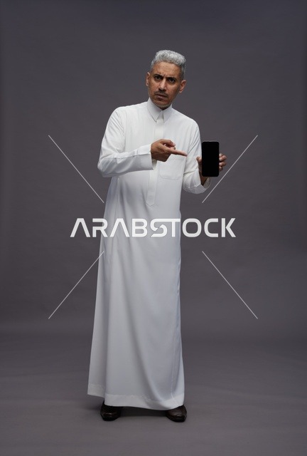 رجل سعودي يشير إلى شاشة هاتف ذكي في الاستوديو