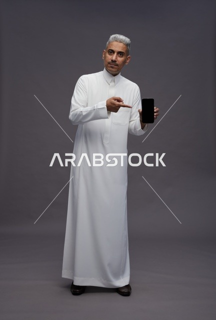 رجل سعودي يشير إلى شاشة هاتف ذكي في الاستوديو