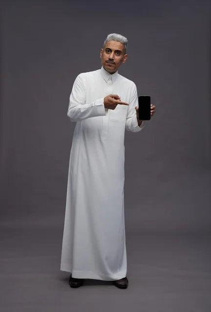 رجل سعودي يشير إلى شاشة هاتف ذكي في الاستوديو
