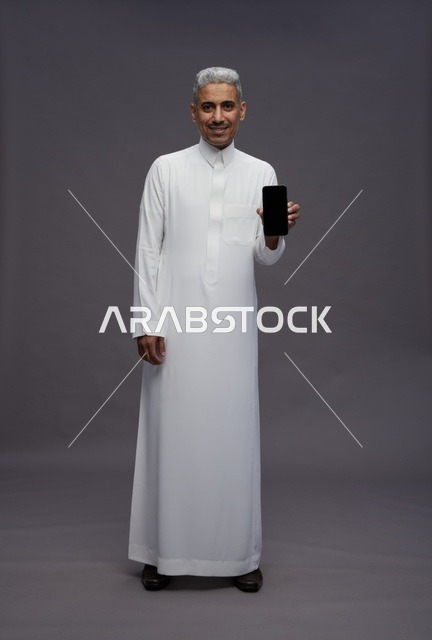 رجل سعودي بالثوب التقليدي يحمل هاتفاً ذكياً
