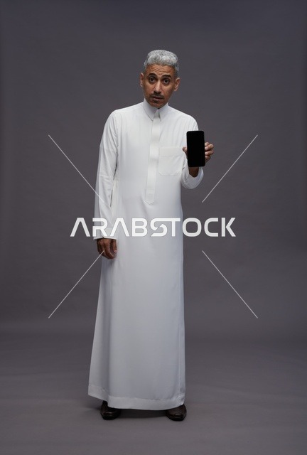 رجل سعودي بالثوب يحمل هاتفاً ذكياً في الاستوديو