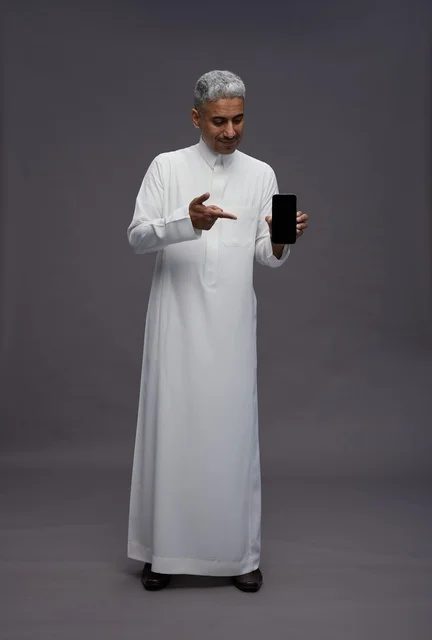 رجل سعودي يشير إلى هاتف ذكي بخلفية رمادية