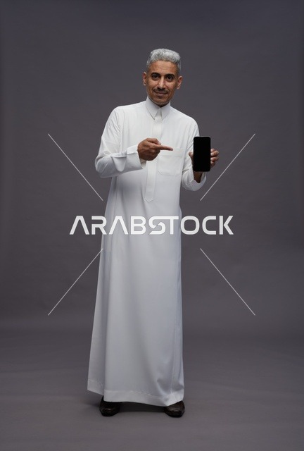 رجل سعودي يرتدي الثوب يحمل هاتفاً ذكياً