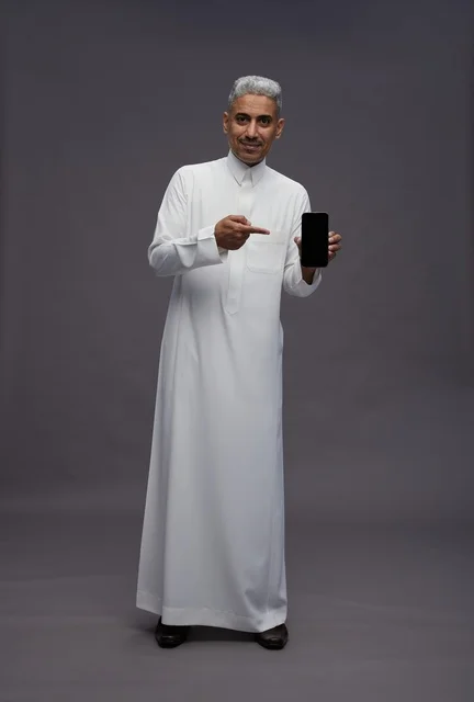 رجل سعودي يرتدي الثوب يحمل هاتفاً ذكياً