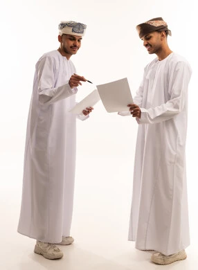 رجال عمانيون بالزي التقليدي يراجعون الوثائق