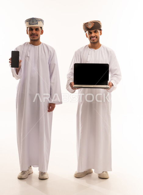 رجلان عمانيان يحملان لابتوب وهاتف ذكي بخلفية بيضاء