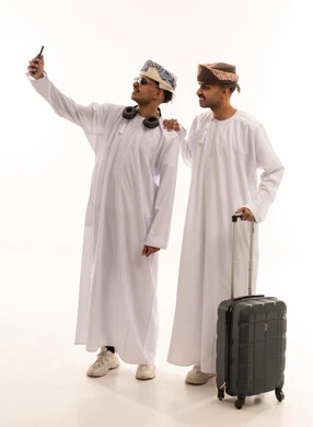 رجال عمانيون بالزي التقليدي يلتقطون سيلفي مع حقيبة سفر