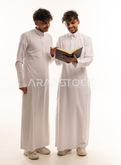 Two Saudi Men in Traditional Thobes Reading a Book
