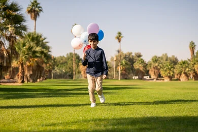 طفل عربي يركض مع بالونات ملونة في الحديقة