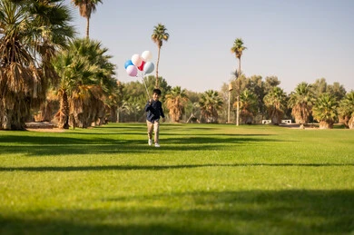 طفل عربي يركض بالبالونات في حديقة عامة