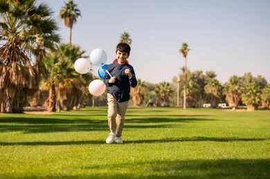 طفل عربي يركض في حديقة خضراء مع بالونات