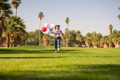 طفلة سعودية تركض في الحديقة مع بالونات ملونة