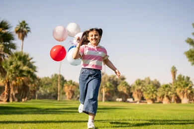 Young Saudi Girl Running with Balloons in Public Park