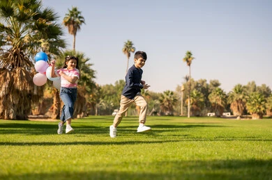 أطفال سعوديون يركضون في الحديقة مع بالونات