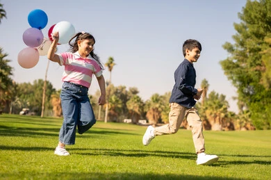 أطفال عرب يركضون بالبالونات في حديقة عامة
