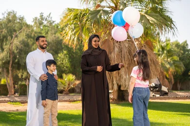 عائلة عربية مع بالونات ملونة في حديقة مشمسة