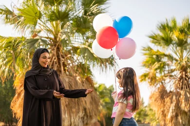 امرأة سعودية مع طفلة تحمل بالونات ملونة في حديقة عامة