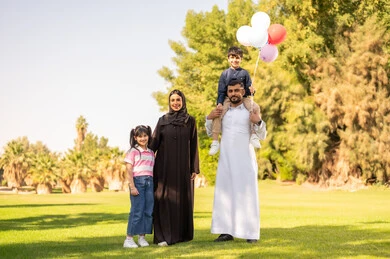 عائلة سعودية مع بالونات في حديقة عامة خضراء