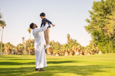 أب سعودي يرفع ابنه في حديقة عامة خضراء