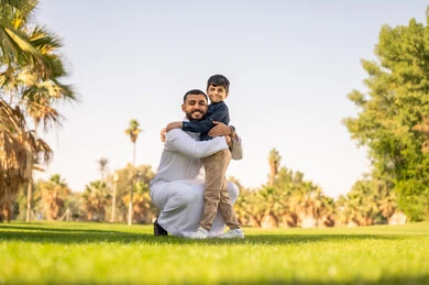 أب إماراتي يحتضن ابنه في حديقة مشمسة