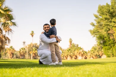 أب إماراتي يحتضن ابنه في حديقة خضراء