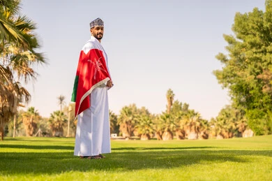 رجل عُماني مع العلم الوطني في حديقة مشمسة