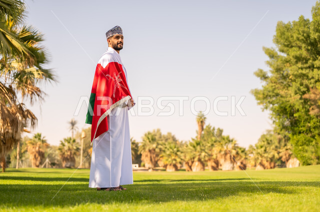 رجل عماني بالزي التقليدي يرتدي علم سلطنة عمان