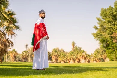 رجل عماني بالزي التقليدي يرتدي علم سلطنة عمان