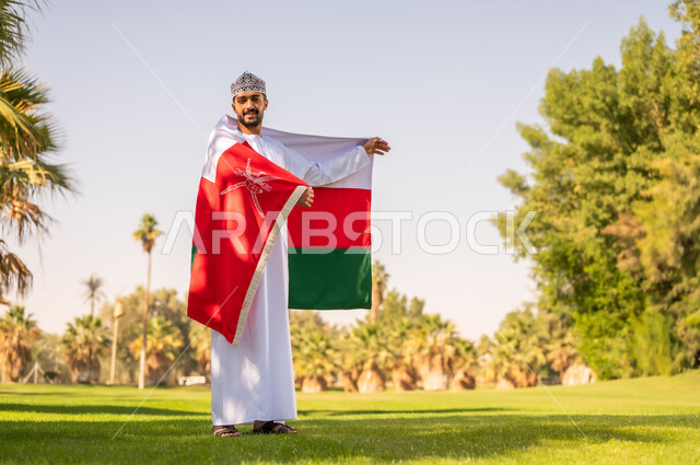 رجل عماني يحمل علم السلطنة في حديقة خضراء