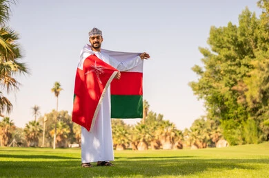 رجل عماني يحمل علم السلطنة في حديقة خضراء