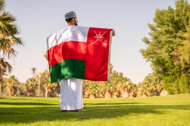 رجل عماني يحمل العلم الوطني في حديقة خضراء