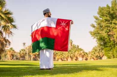 رجل عُماني يحمل علم السلطنة في حديقة خضراء