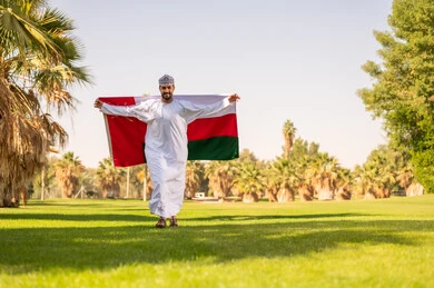 رجل عُماني يحمل العلم الوطني في حديقة خضراء
