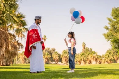 Omani Man with Flag and Girl with Balloons in Park