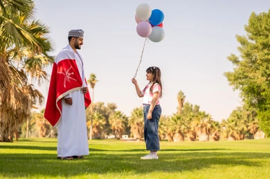 رجل عماني بالعلم وطفلة مع بالونات في الحديقة