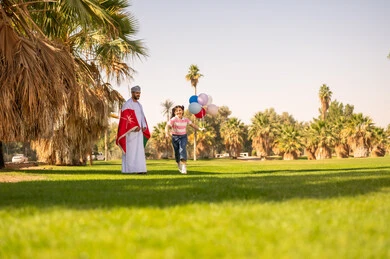 رجل عماني وفتاة مع بالونات في حديقة خضراء