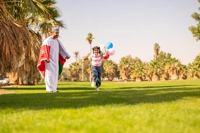 رجل وطفلة يحتفلان بعلم سلطنة عمان في الحديقة