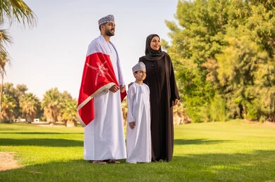 عائلة عمانية بالزي التقليدي مع العلم الوطني في الحديقة